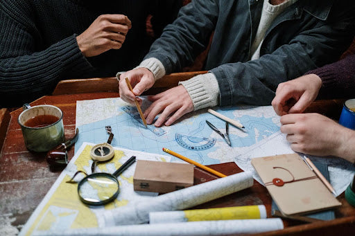 People plotting a route on a paper nautical chart using a parallel ruler, protractor and pencil for navigation.